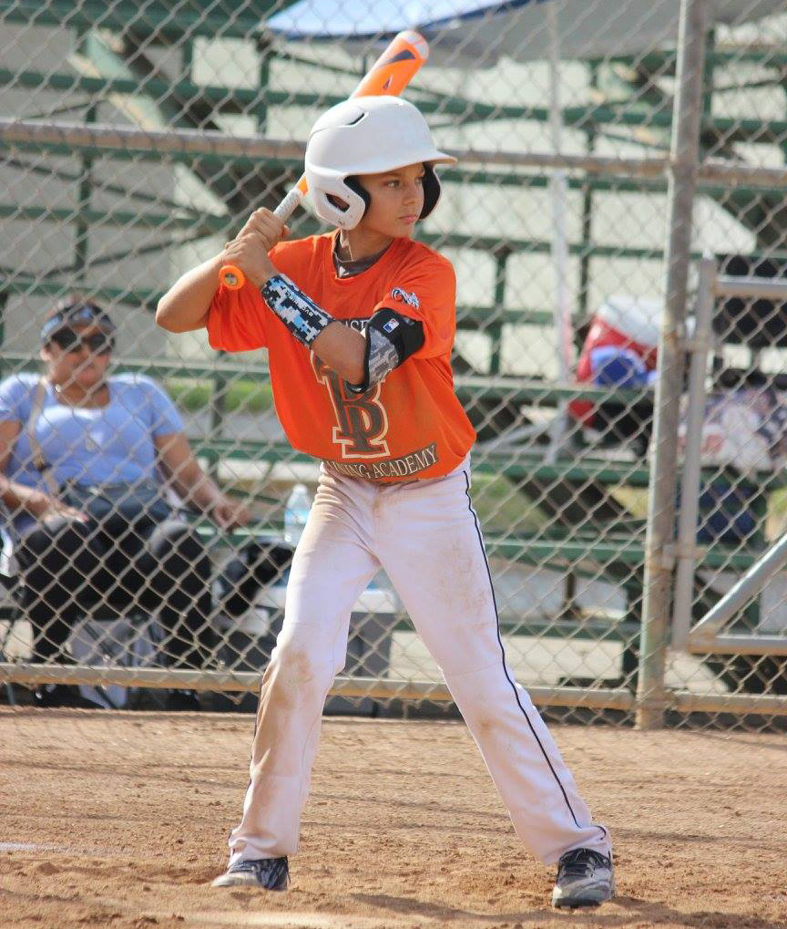 youth baseball player at bat wearing white pants orange jersey and white helmet