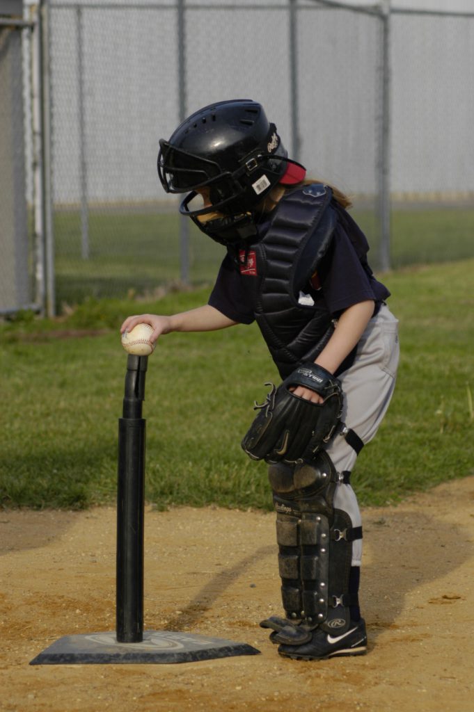 catcher placing a baseball on a tee